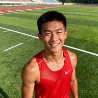 一位25岁左右的男性短跑运动员，短发，穿着运动背心，表情自信微笑，背景为田径场